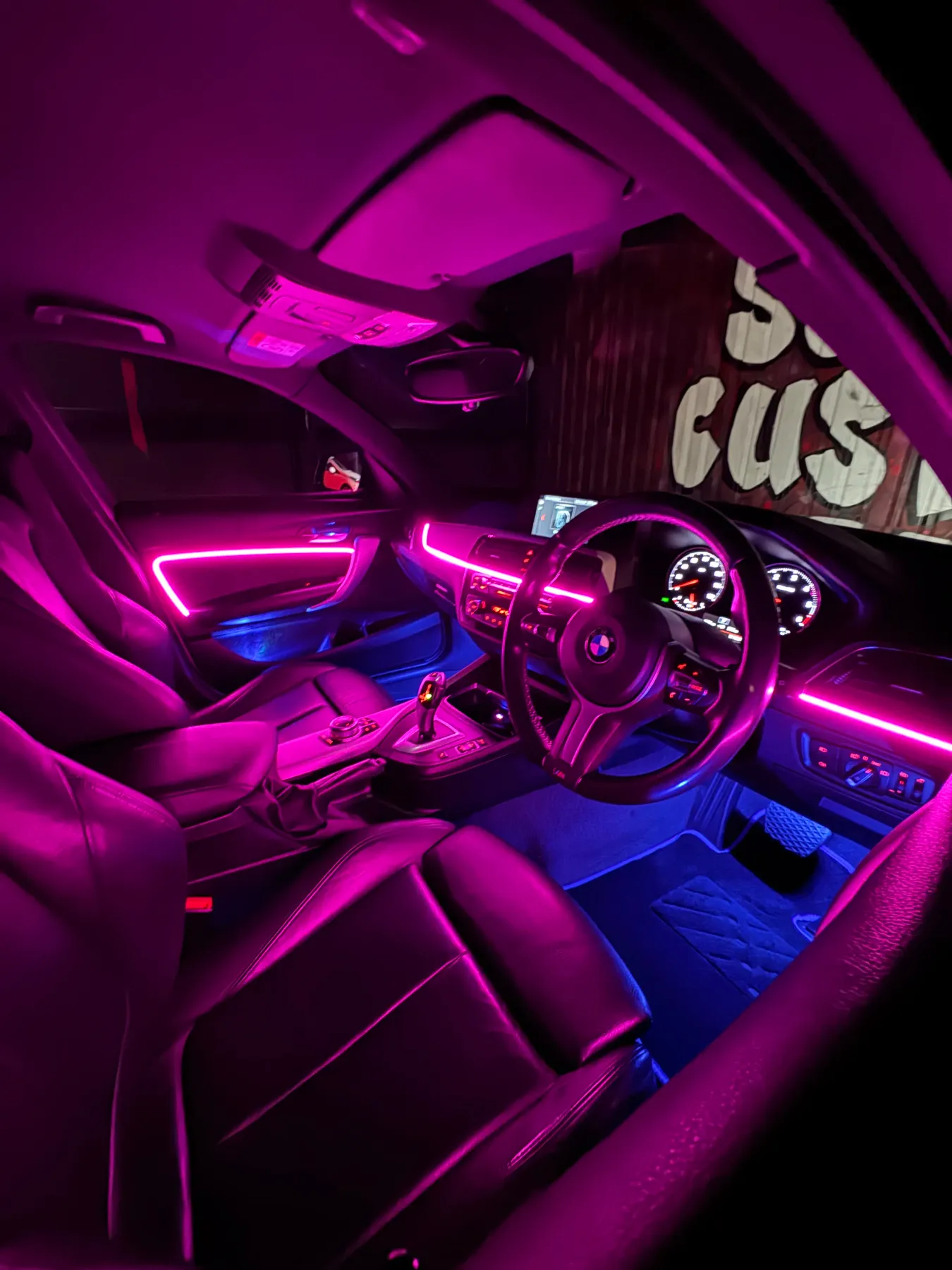 BMW interior glowing with pink ambient lighting across the dashboard and doors.